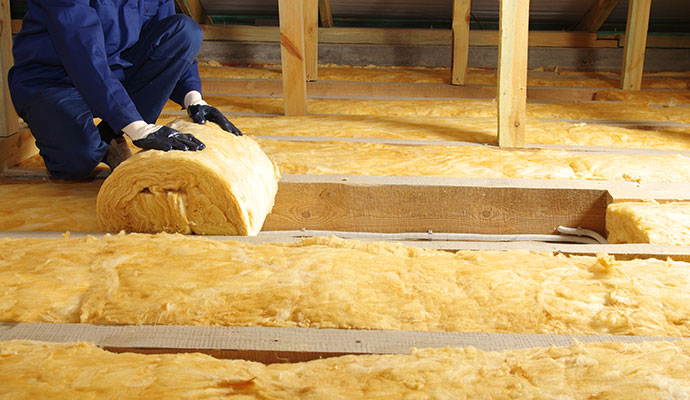 Worker installing new fiberglass insulation rolls in an attic