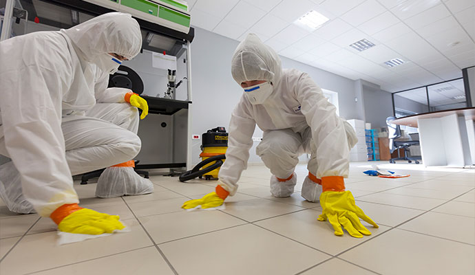Biohazard remediation specialists cleaning tiled floor in protective suits and gloves