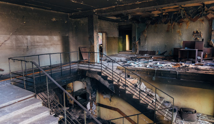 Fire damaged commercial building interior with soot covered walls and charred staircase