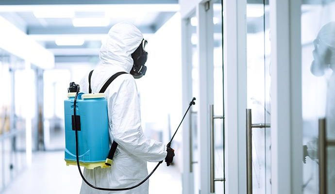 Technician in hazmat suit spraying disinfectant in a commercial office hallway