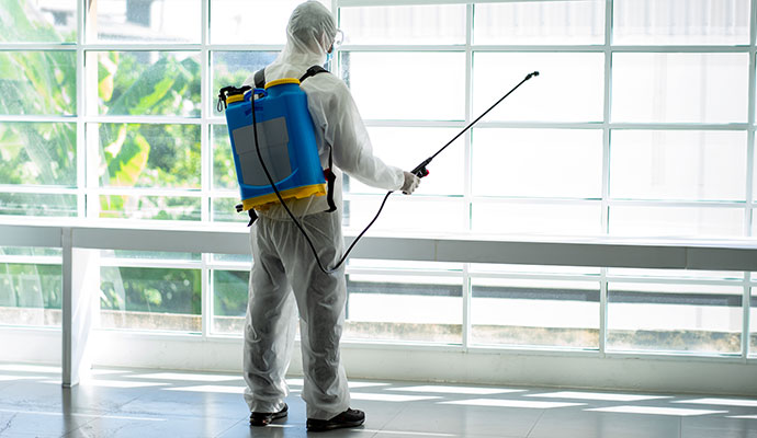 Technician in protective gear spraying disinfectant in a building hallway