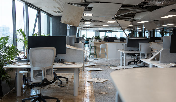 Office workspace damaged by storm with collapsed ceiling tiles and debris