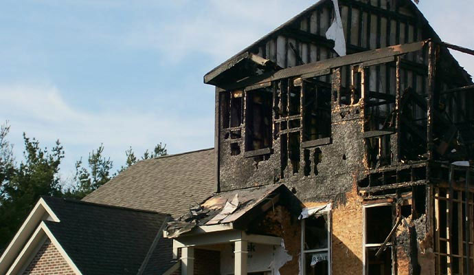Residential house exterior with severe structural fire damage and charred framing
