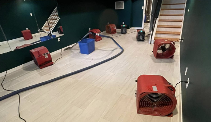 Indoor water damage drying process with air movers hoses and restoration equipment placed throughout basement area